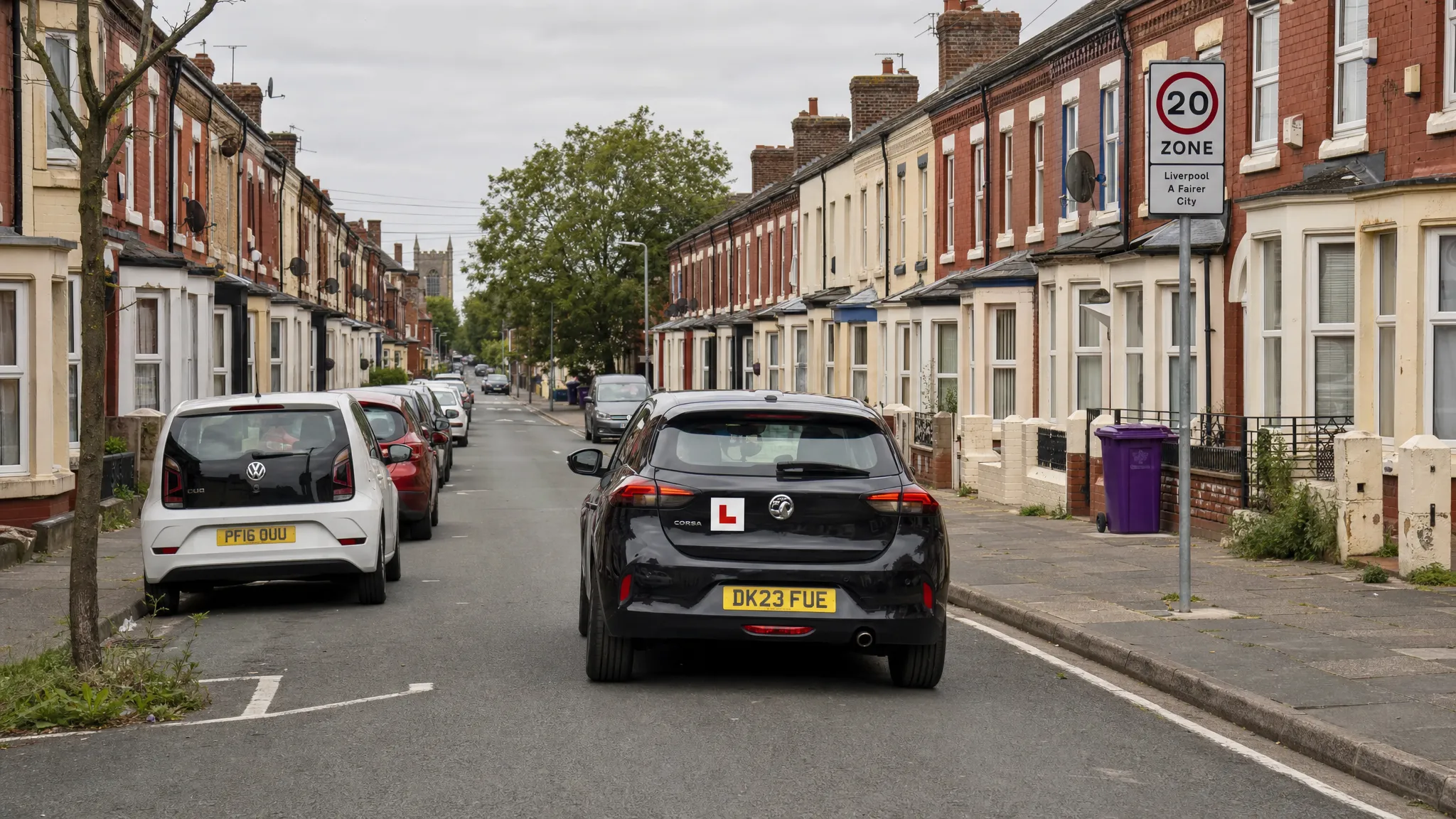 A learner car travelling along a Liverpool residential street with parked cars, terraced houses and clear road markings, showing a calm setting for early driving practice.